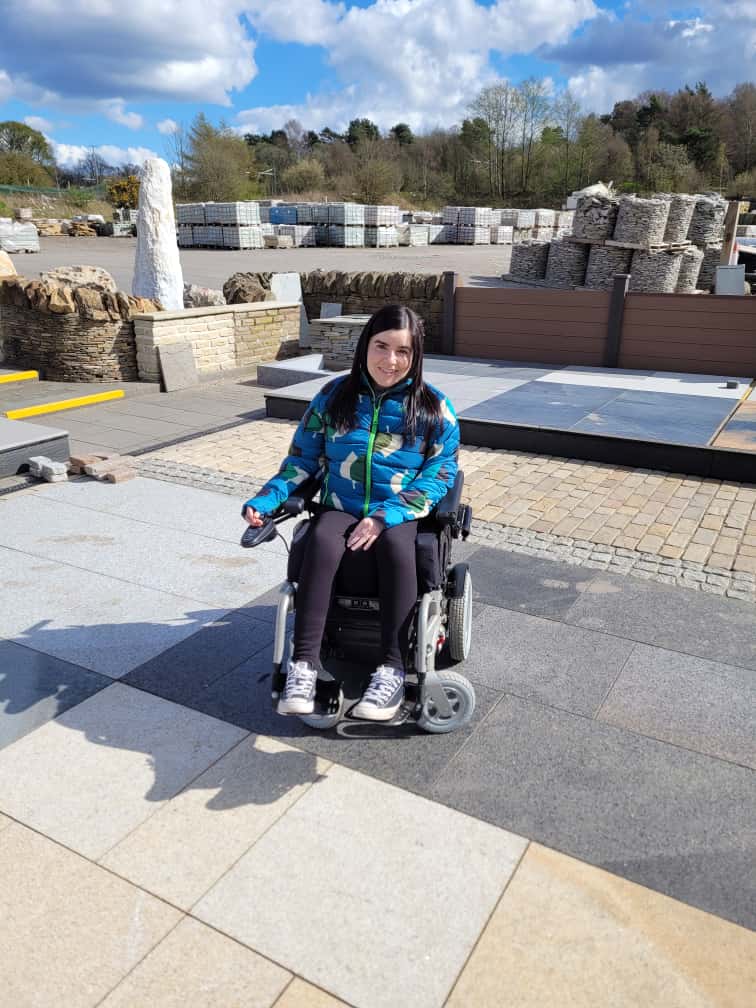 Emma, a wheelchair user, is at a landscape merchants looking at paving stones.