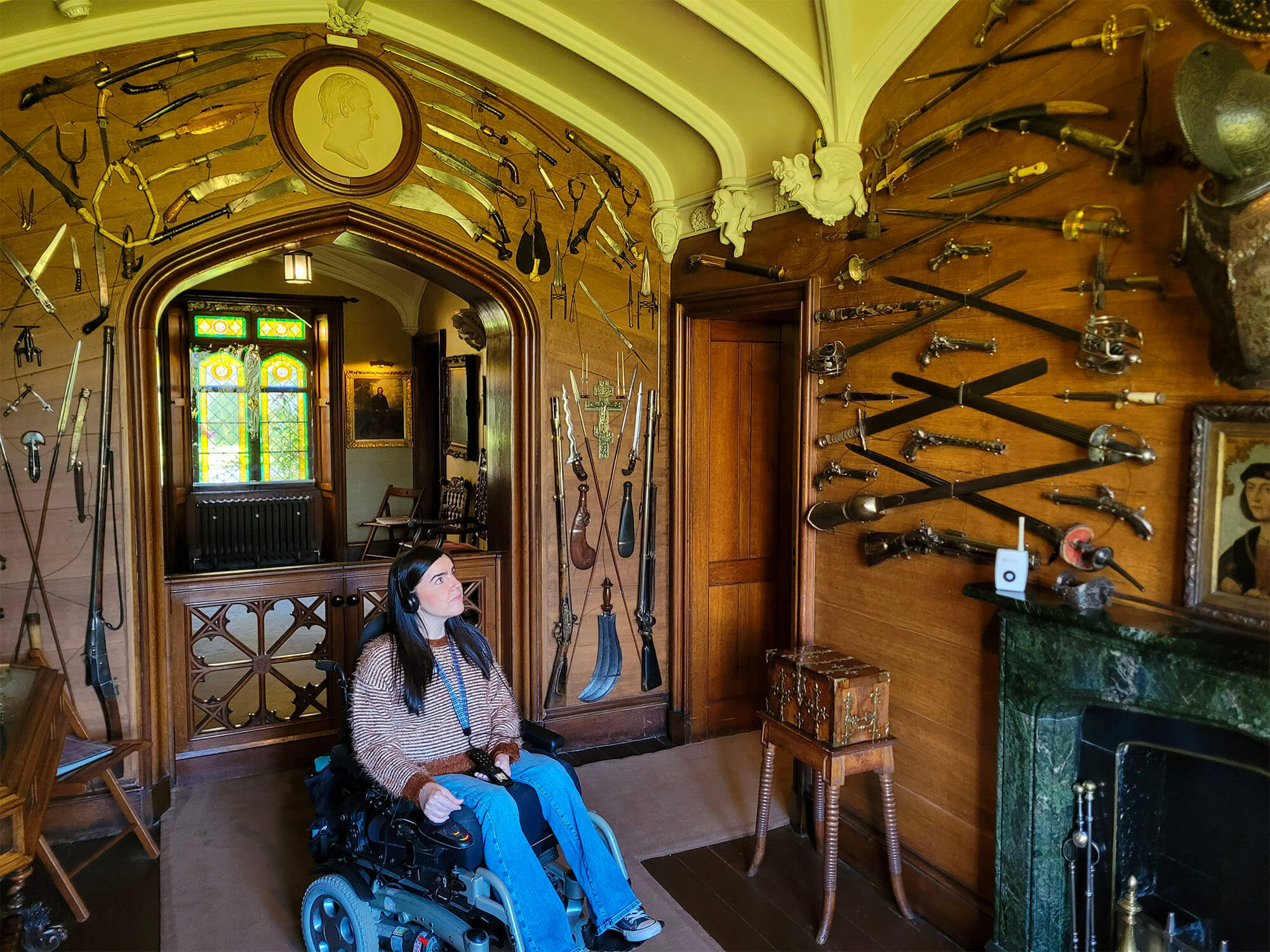Emma, a power wheelchair user is wearing headphones for the audio tour and she is in the armoury and weapons room at Abbotsford House.