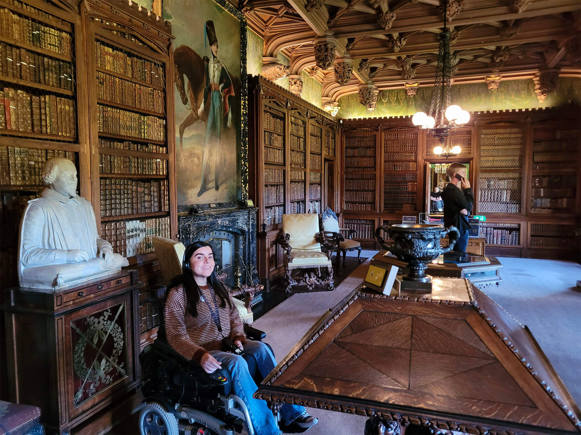 Emma, a power wheelchair user is wearing headphones for the audio tour and she is in the library at Abbotsford House.
