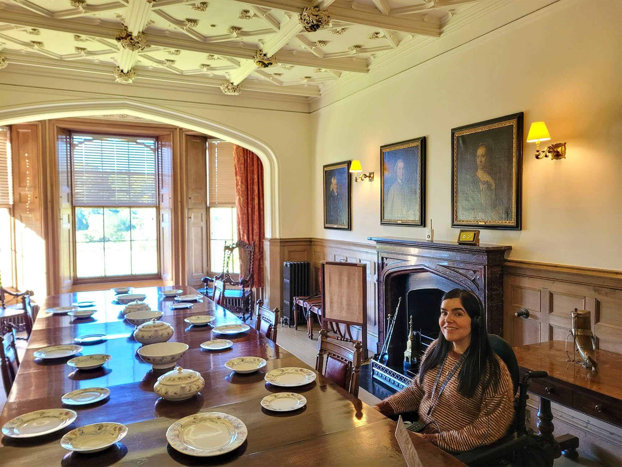 Emma is sitting at the dining table in the dining room of Abbotsford, the home of Sir Walter Scott. She is smiling at the camera.