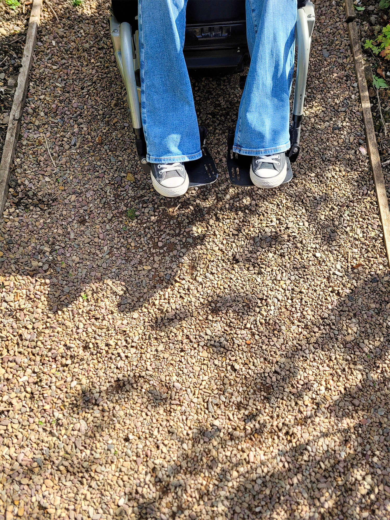 A close up of Emma's lower legs and feet on her wheelchair footplates and the smooth resin-bound gravel that she is driving over.