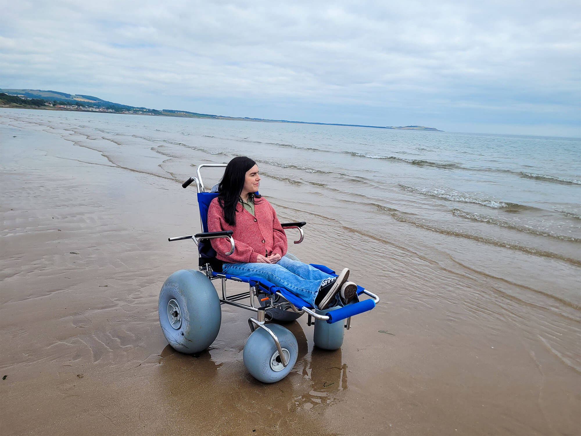 Emma sat in a manual sandcruiser with balloon wheels from Silverburn Park Beach Wheelchairs.