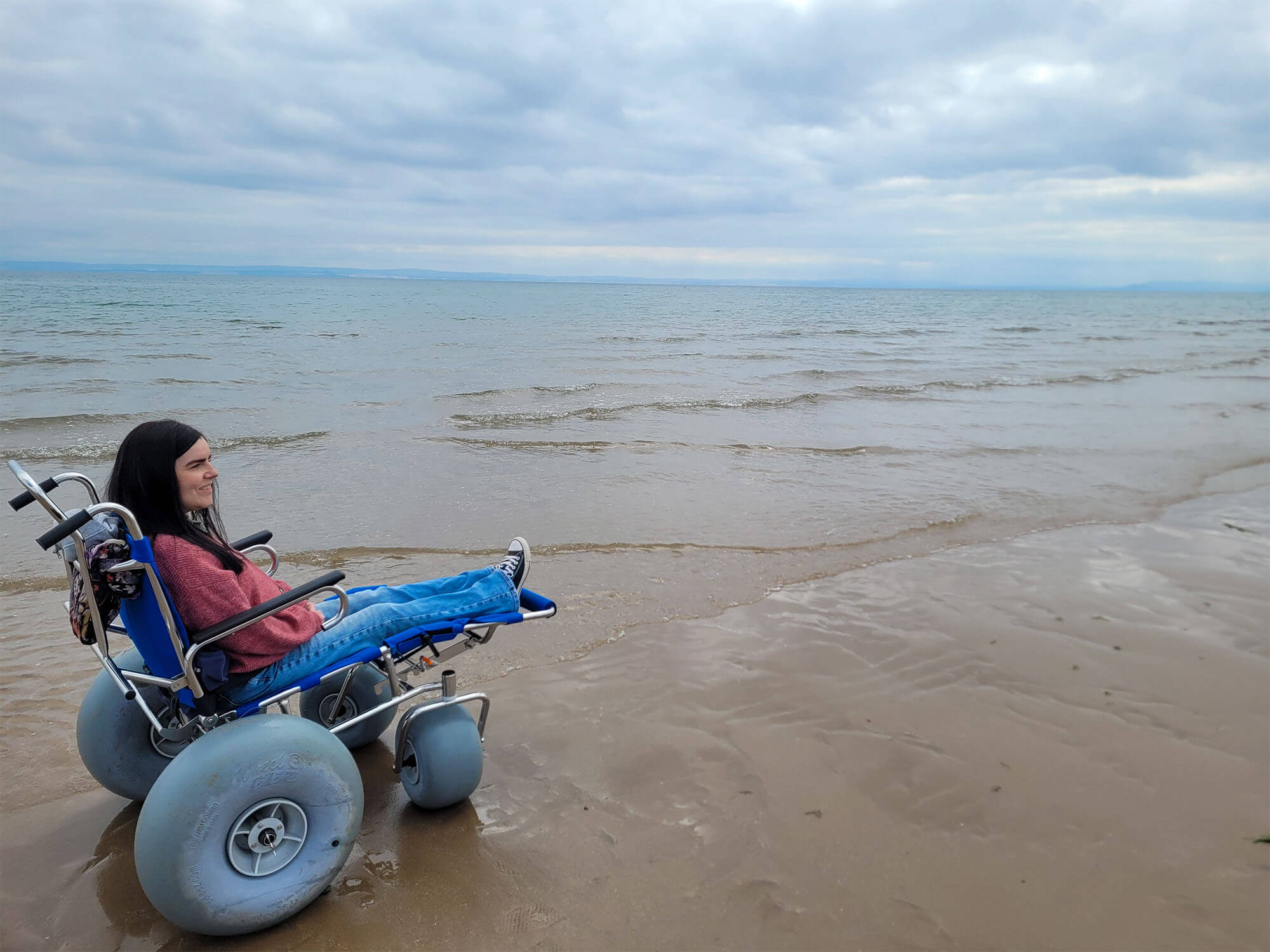Emma sat in a manual sandcruiser with balloon wheels from Silverburn Park Beach Wheelchairs.
