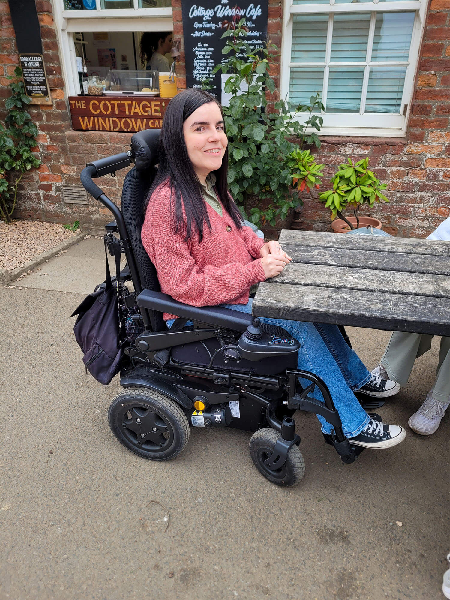 Emma sitting at the wheelchair accessible picnic table at The Cottage Window Café in Silverburn Park, Fife.