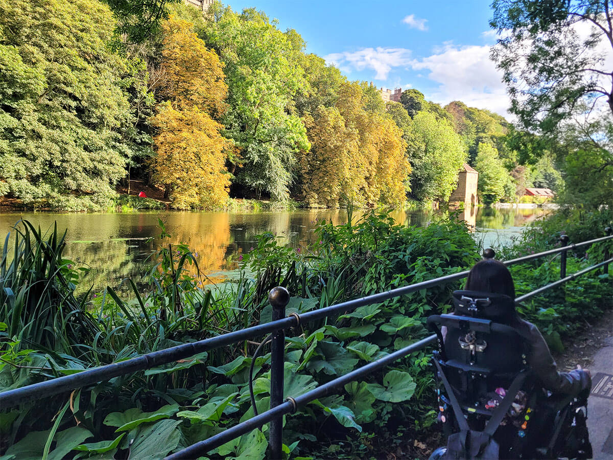 Emma, driving in her wheelchair alongside the River Wear lined with lush green trees that are beginning to show signs of autmn