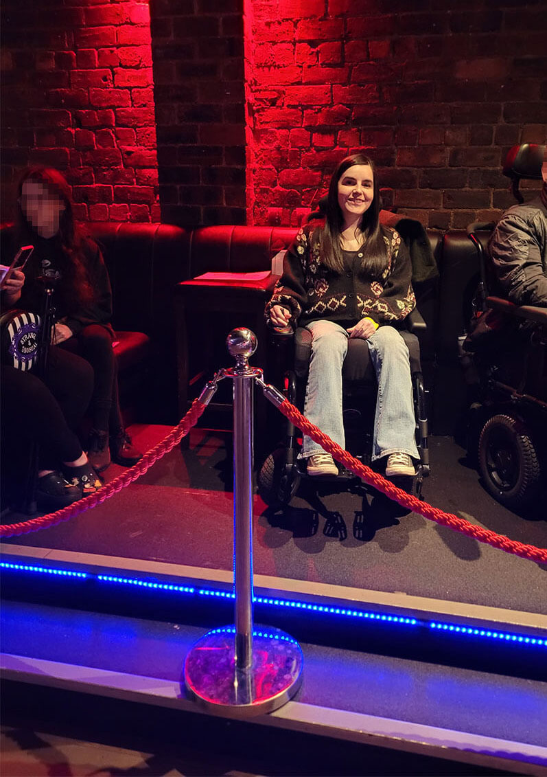 Emma sitting in her wheelchair on the raised viewing platform at The Garage, Glasgow.