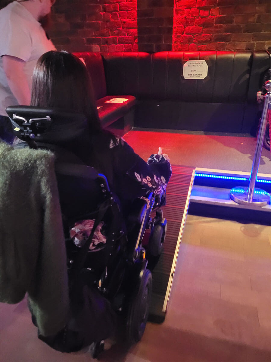 Emma driving her wheelchair up the portable ramp on to the raised viewing platform at The Garage, Glasgow.